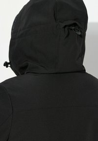 Giacca nera impermeabile con cappuccio aderente e cordini regolabili, caratterizzata da una superficie liscia e opaca. I dettagli delle cuciture sono visibili sulla schiena.
