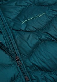 Giacca a piumino turchese con design trapuntato, dotata di zip completa e "PeakPerformance" ricamato in verde sul petto.