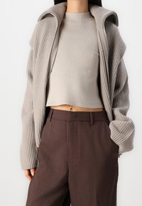 Maglione corto a coste beige con un motivo testurizzato, abbinato a pantaloni marroni a vita alta con finitura liscia e tasche laterali.