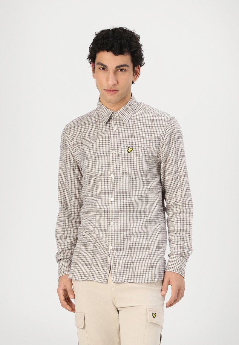 Brązowa i biała koszula w kratę z guzikiem, z kołnierzykiem i żółtym haftowanym logo na piersi. Slim fit, długie rękawy i bawełniany materiał.