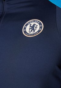 Giacca da football blu navy con una finitura testurizzata. Presenta un logo circolare del Chelsea Football Club in ricamo bianco e oro sul petto.