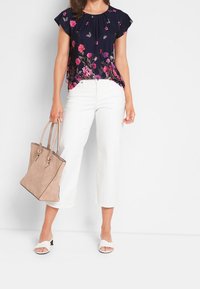 Mörkblå blus med blommönster och korta ärmar, kombinerad med vita vida byxor, håller en beige toteväska och bär vita klacksandaler.