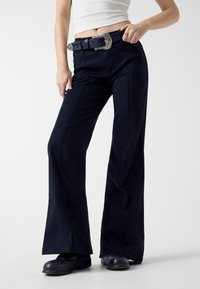 Granatowe spodnie o szerokich nogawkach wykonane z gładkiej tkaniny, z bocznymi szwami, paskiem z ozdobną srebrną klamrą oraz dopasowaną talią.