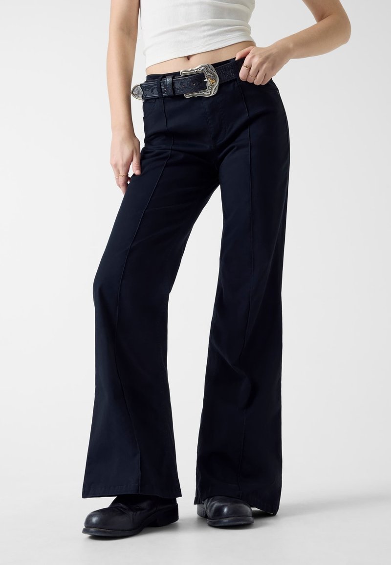 Granatowe spodnie o szerokich nogawkach wykonane z gładkiej tkaniny, z bocznymi szwami, paskiem z ozdobną srebrną klamrą oraz dopasowaną talią.
