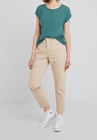 Grön t-shirt med korta ärmar kombinerad med beige högmidjade jeans och vita sneakers; avslappnad passform, mjukt tyg, enkel design.