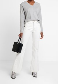 Šedý svetr s výstřihem do V, bílé rozšířené džíny, černá kabelka s krátkými uchy a šedé kotníkové boty s hadím vzorem. Jednoduchý, ležérní outfit.