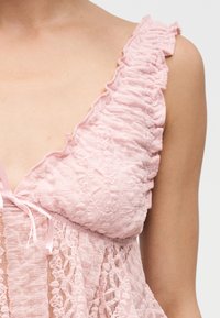 Ροζ δαντελένιο ρούχο χωρίς μανίκια με βολάν στους τιράντες και υφή, αποκαλύπτοντας μερικώς τον ώμο και το πάνω μέρος του στήθους.