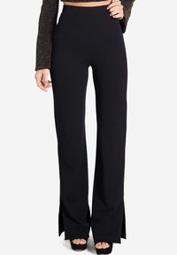 Pantalons évasés noirs taille haute avec fentes latérales, fabriqués en tissu extensible. Texture lisse, ajustés au niveau des hanches, design à jambes larges.