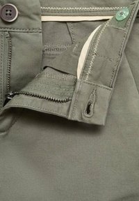 Pantaloni verde oliva con zip e chiusura a bottone, vita color crema e dettagli di cucitura a contrasto. Materiale in cotone strutturato.