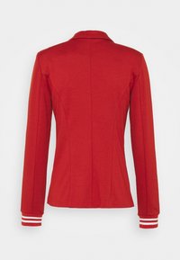 Veste rouge à manches longues avec un col montant et des doubles rayures blanches aux poignets, vue de dos sur un fond uni.