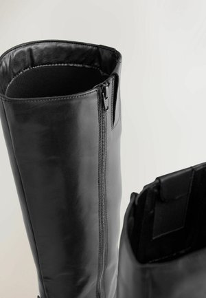 Cizme negre din piele până la genunchi, cu suprafață netedă, fermoar lateral și căptușeală interioară moale. Au vârf rotunjit și accente minimaliste.