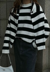 Gestreifter Strickpullover in Schwarz und Weiß mit oversized Passform, gerippten Bündchen und Rundhalsausschnitt, kombiniert mit einem dunklen Jeansrock und einer weißen Handtasche.