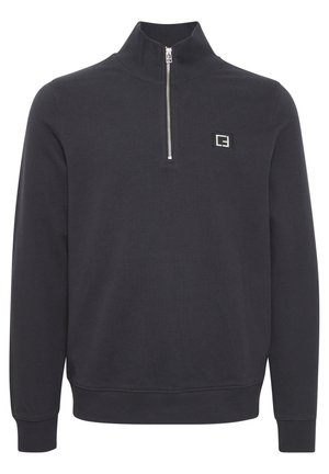 Juodas ketvirtuko zipas megztinis, pagamintas iš minkštos medžiagos. Yra mažas logotipo aplikacija kairėje pusėje ir raukšlėtos rankovės ir apatinės krašto dalys.