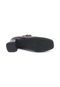 Zapato de tacón alto burdeos con un acabado brillante, que cuenta con un acento decorativo de cadena dorada y una suela de goma negra texturizada.