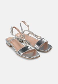 Zilveren metallic sandalen met een platte vierkante neus, verstelbare enkelband en met kralen versierde detail dat de band en de zool verbindt.
