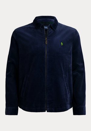 Marineblauw corduroy jack met een rits aan de voorkant, kraag en twee zijzakken. Heeft een klein groen logo op het linkerborstgebied.