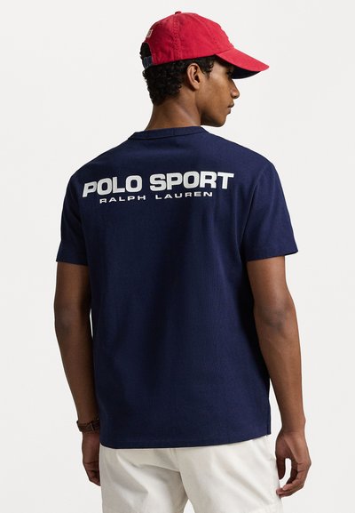Tamsiai mėlyna trumpomis rankovėmis marškinėliai, kuriuose ant nugaros yra baltas tekstas "POLO SPORT RALPH LAUREN". Pagaminti iš medvilnės, su laisvu siluetu.