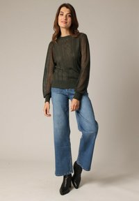 Groene gebreide trui met doorzichtige pofmouwen, voorzien van verticale ribbels en ruitpatronen. Gecombineerd met brede blauwe jeans en zwarte enkellaarsjes.