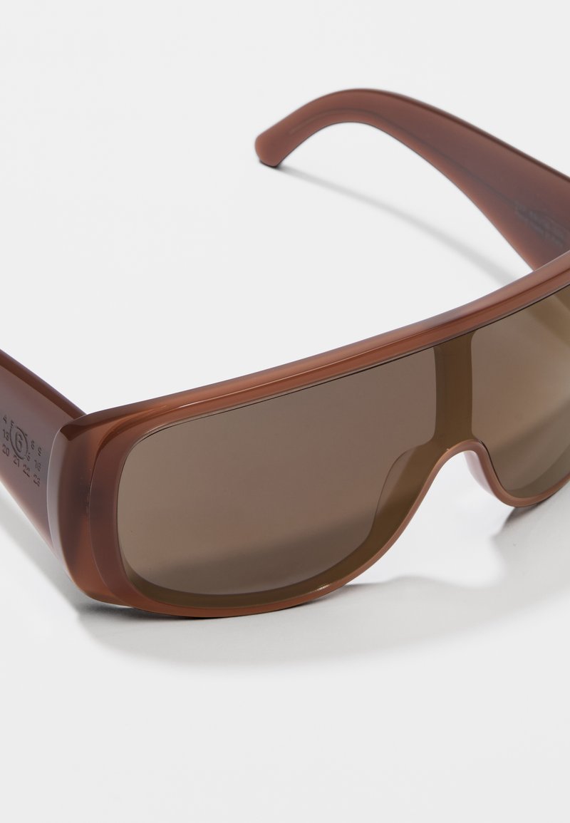 Braune Kunststoffsonnenbrille mit einem Wraparound-Design, dunklen Gläsern und glatter Textur sowie dezenter Markenkennzeichnung an den Bügeln.