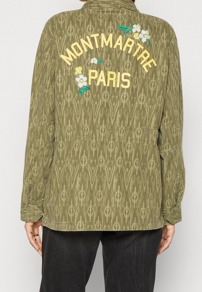 Olijfgroene jas met een ikatpatroon, voorzien van bloemenborduursel en "MONTMARTRE PARIS" in het geel op de rug. Relaxte pasvorm en lange mouwen.