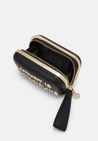 Czarna skórzana torba z złotym zamkiem i metalowymi literami na przodzie. Posiada okrągły uchwyt zamka i gładką teksturę z wewnętrzną komorą.