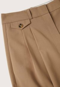 Pantalons ajustés beiges avec une finition plate, des plis sur le dessus et une fermeture à bouton unique. Fabriqués en tissu lisse avec un design structuré.