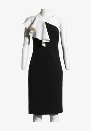 Robe noire asymétrique avec un grand volant blanc sur l'épaule gauche, longueur genou, sur un mannequin sans bras.