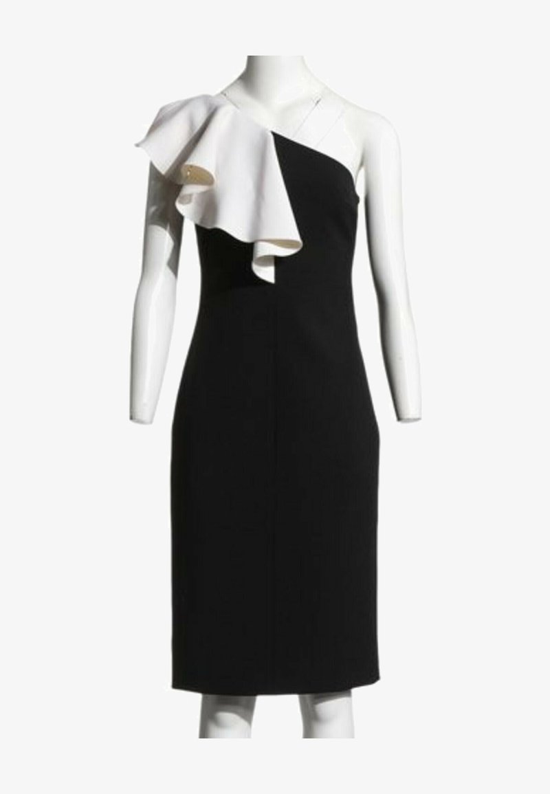 Robe noire asymétrique avec un grand volant blanc sur l'épaule gauche, longueur genou, sur un mannequin sans bras.