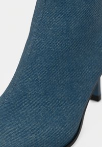 Denim ankelstøvler med et teksturert blått stoff, spiss tå og en slank svart hæl, med en glatt og sømløs design.