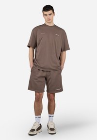 Brun bomull t-skjorte og matchende shorts med en avslappet passform. Merkevarelogo på shortsen. Kombineres med beigefargede og mørkebrune sneakers.