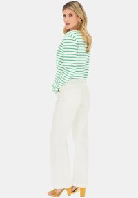 Białe szerokie spodnie połączone z zieloną i białą w paski koszulą z długim rękawem. Koszula ma okrągły dekolt i dopasowane rękawy.