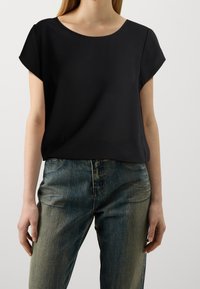 Top nero a maniche corte con scollatura rotonda, realizzato in tessuto liscio, abbinato a jeans a vita alta blu chiaro, leggermente strutturati.