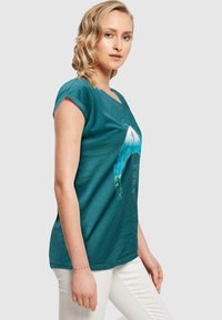Teal katoenen t-shirt met een ronde hals, korte mouwen en een grafisch ontwerp met onderwaterelementen en het woord "MERA."