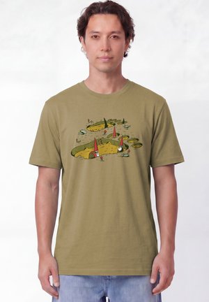 Homme portant un t-shirt vert olive avec des gnomes dessinés creusant des trous et grimpant des échelles sur le devant.