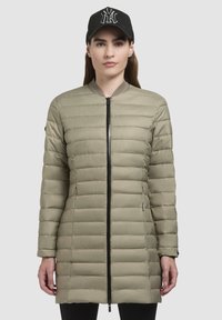 Kaki puffjacka med horisontell quiltning, slim fit, hög krage och frontdragkedja. Kompletteras av en svart basebollkeps med vitt logotyp.