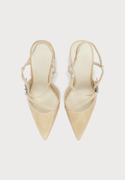 Talons slingback beige à bout pointu avec fines lanières croisées et une petite boucle argentée, vus de dessus sur fond blanc.