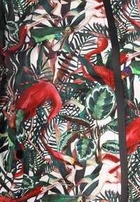 Farverig lynlåsjakke med et botanisk print med røde flamingoer, forskellige fugle og grønne blade på en hvid baggrund.
