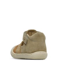 Beige semišová bota s suchým zipem, kulatou špičkou a vystříhaným designem. Podešev je texturovaná, což zajišťuje přilnavost a podporu.