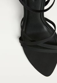 Schwarze High-Heel-Sandalette mit spitzem Zeh, ausgestattet mit mehreren dünnen Riemen und einem strukturierten Fußbett, das eine elegante Silhouette erzeugt.