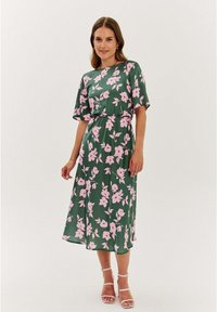 Zelené kvetinové šaty s ružovými kvetmi, krátkymi rukávmi, sťahovaným pásom a stredne dlhým lemom. Hladká tkanina a voľný strih. Minimálne kovové doplnky.