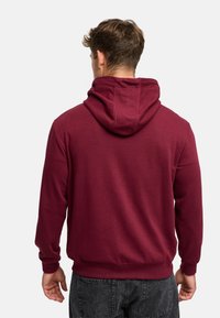 Burgundowa bluza z kapturem, ze sznurkiem, ściśniętymi mankietami i dołem. Gładka faktura, luźny krój i duży kaptur z tyłu. Standardowa kieszeń typu pouch.