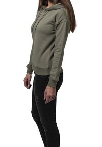 Sudadera con capucha verde oliva con bolsillo tipo canguro, capucha con cordón, puños y dobladillo acanalados. Combinada con pantalones vaqueros pitillo negros desgastados.