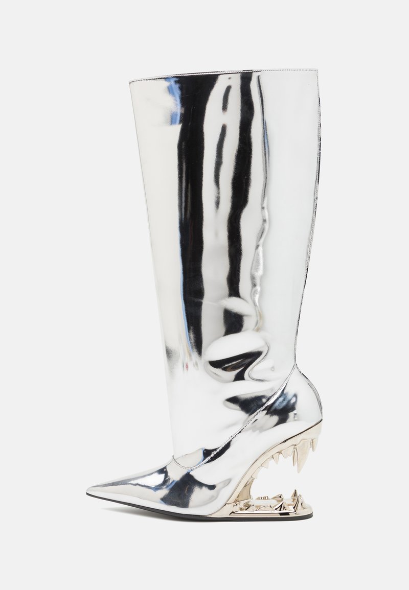 Shiny silver knee-high boot with a pointed toe, featuring a sculptural heel resembling a jagged design. Smooth, reflective surface.