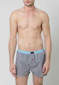 Boxerské šortky mají námořnickou a bílou kostkovanou vzor, světlomodrý elastický pás a malý červený knoflíkový detail vepředu.