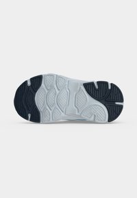 Semelle d'une chaussure de sport blanche et noire avec des motifs texturés offrant adhérence et flexibilité sur un fond clair uni.