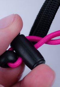 Schwarzer Kordelstopper sichert eine leuchtend pinke Schnur, gehalten zwischen Zeigefinger und Daumen, mit gewebtem Texturdetails an Schnur und Stopper.