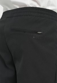 Zwarte broek van een soepel, textuurrijk materiaal. Bevat een achterzak met ritssluiting en een tonale "BOSS"-logo nabij de tailleband.