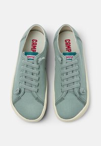 Sneakers in tela verde chiaro con punta arrotondata, suola in gomma bianca e sistema di allacciatura con sei occhielli. Presentano un logo rosso e blu sulla linguetta.