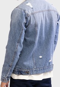 Jasnoniebieska kurtka dżinsowa z efektem postarzania, z detalami przetarć, zapięciem na guziki i spiczastym kołnierzem. Widoczne szwy i kieszenie.