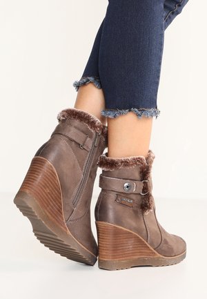 Bottines compensées marron à la cheville avec bordure en fausse fourrure et fermeture éclair, portées avec un jean foncé à ourlet effiloché.